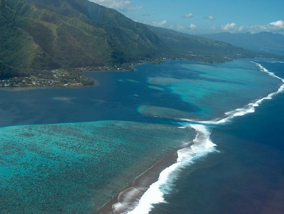 Survol de l'île de Tahiti par la côte ouest, avec le lagon, le récif et la haute-mer (l'océan). Au premier plan : la grande partie de Tahiti : Tahiti Nui. Dans l'arrière plan : la petite partie de l'île appelée Tahiti Iti. Et dans l'isthme : la ville de Taravao.